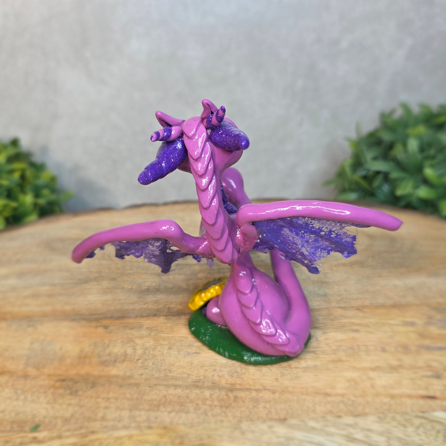A clay dragon figurine on a wooden surface with a blurred green plant in the background