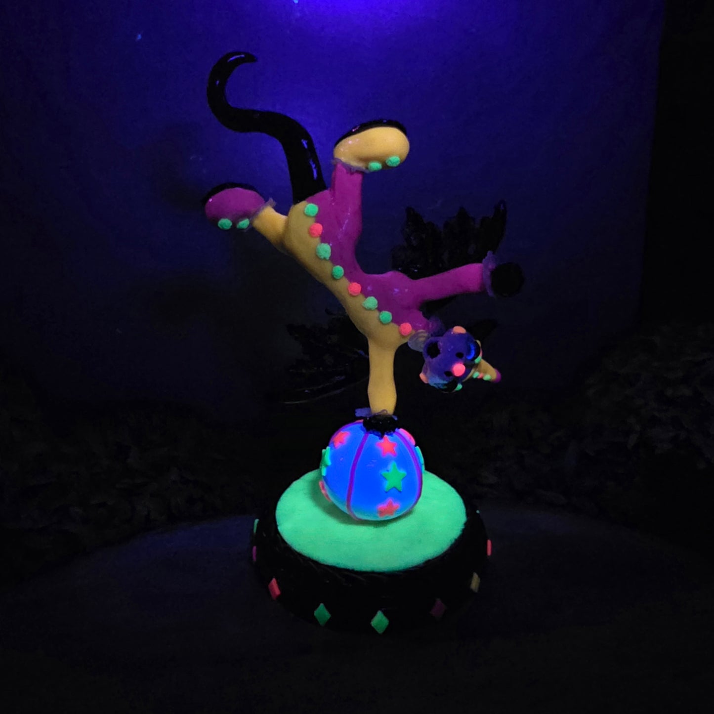 A blacklight reactive clown dragon balancing on a ball on a wood surface with greenery