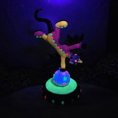 A blacklight reactive clown dragon balancing on a ball on a wood surface with greenery