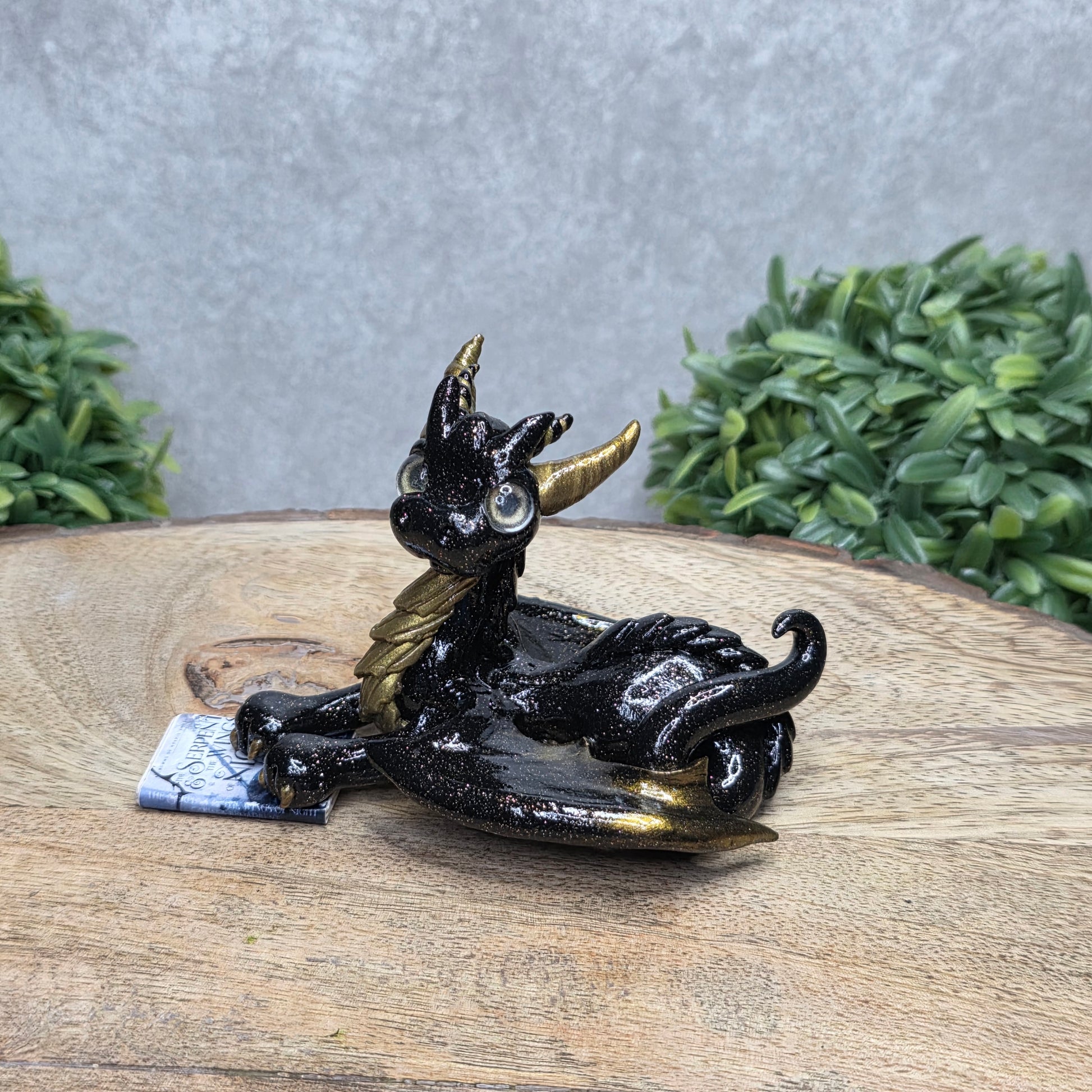 A dragon reading a book against a wood surface with greenery