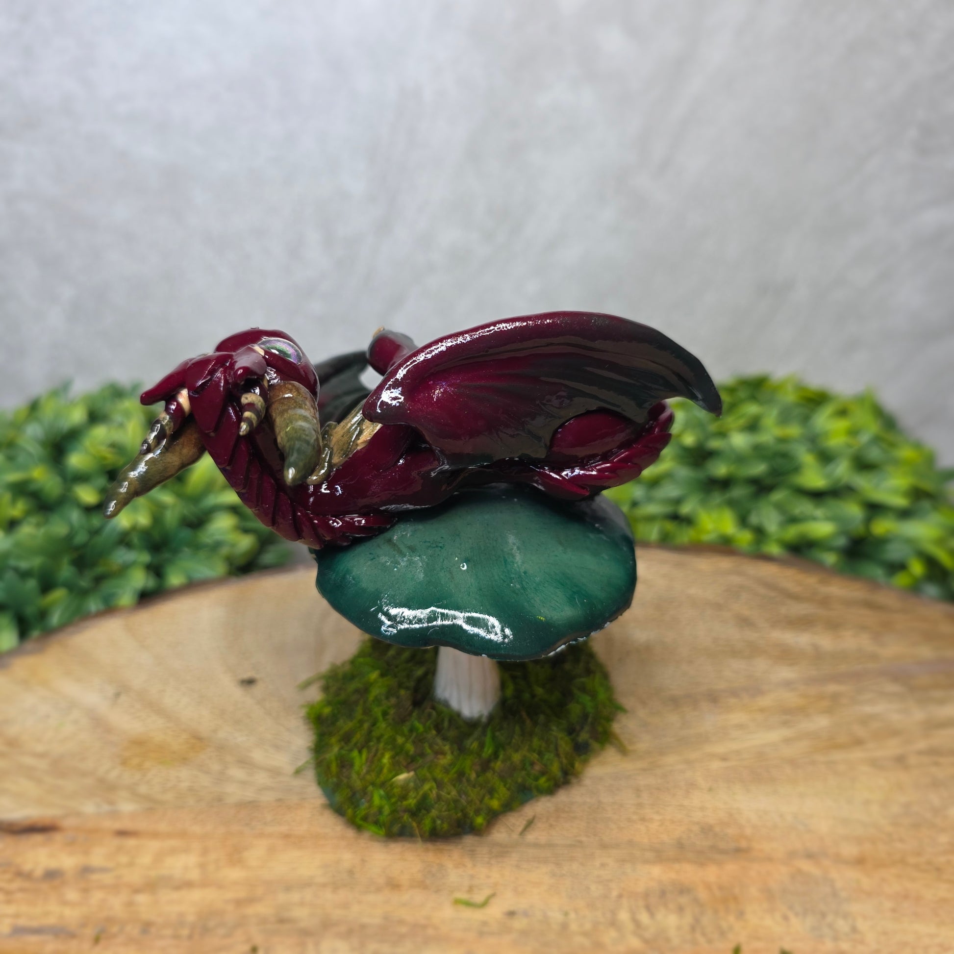 Small dragon figurine on a wooden surface with greenery