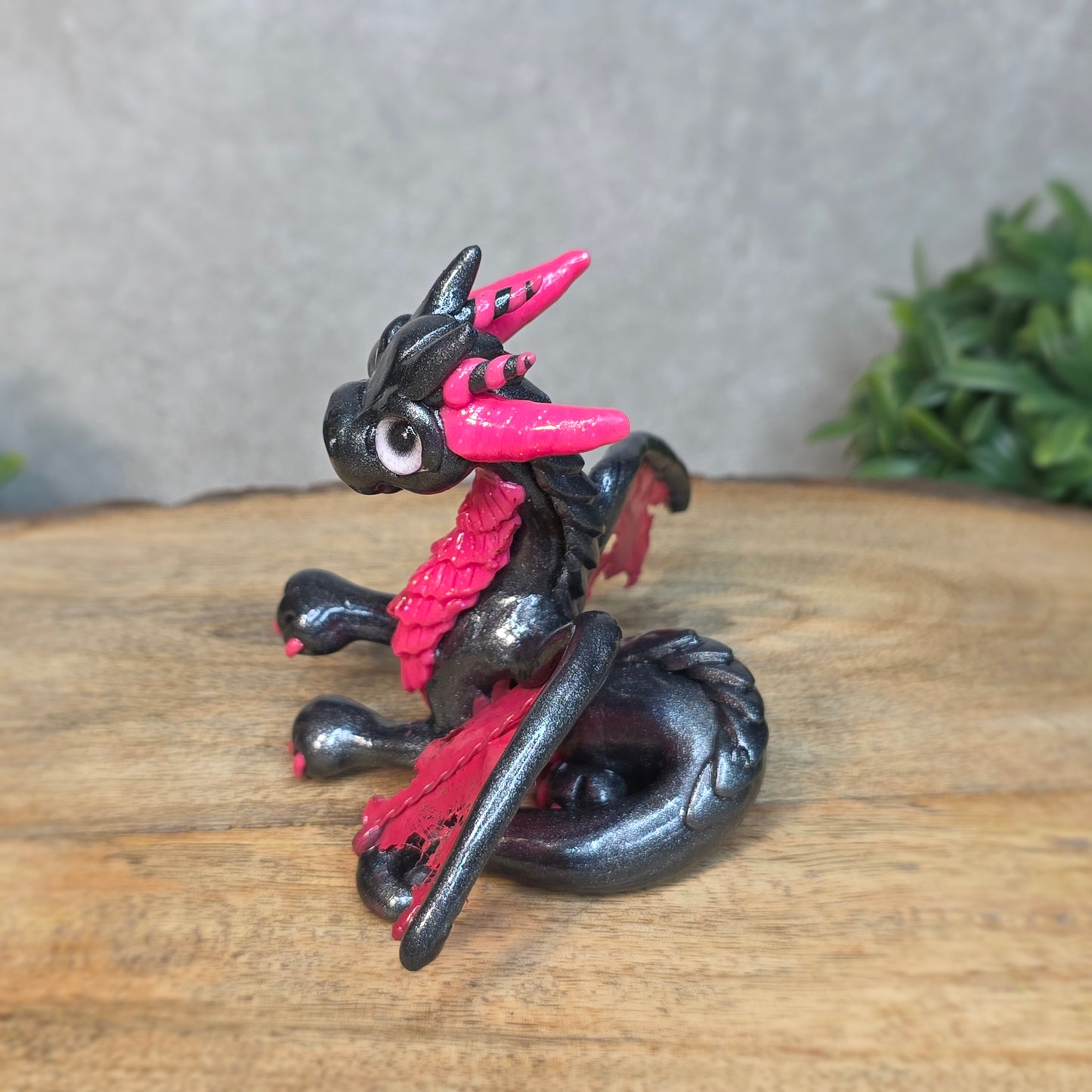 A graphite and pink clay dragon against a blurred wood surface
