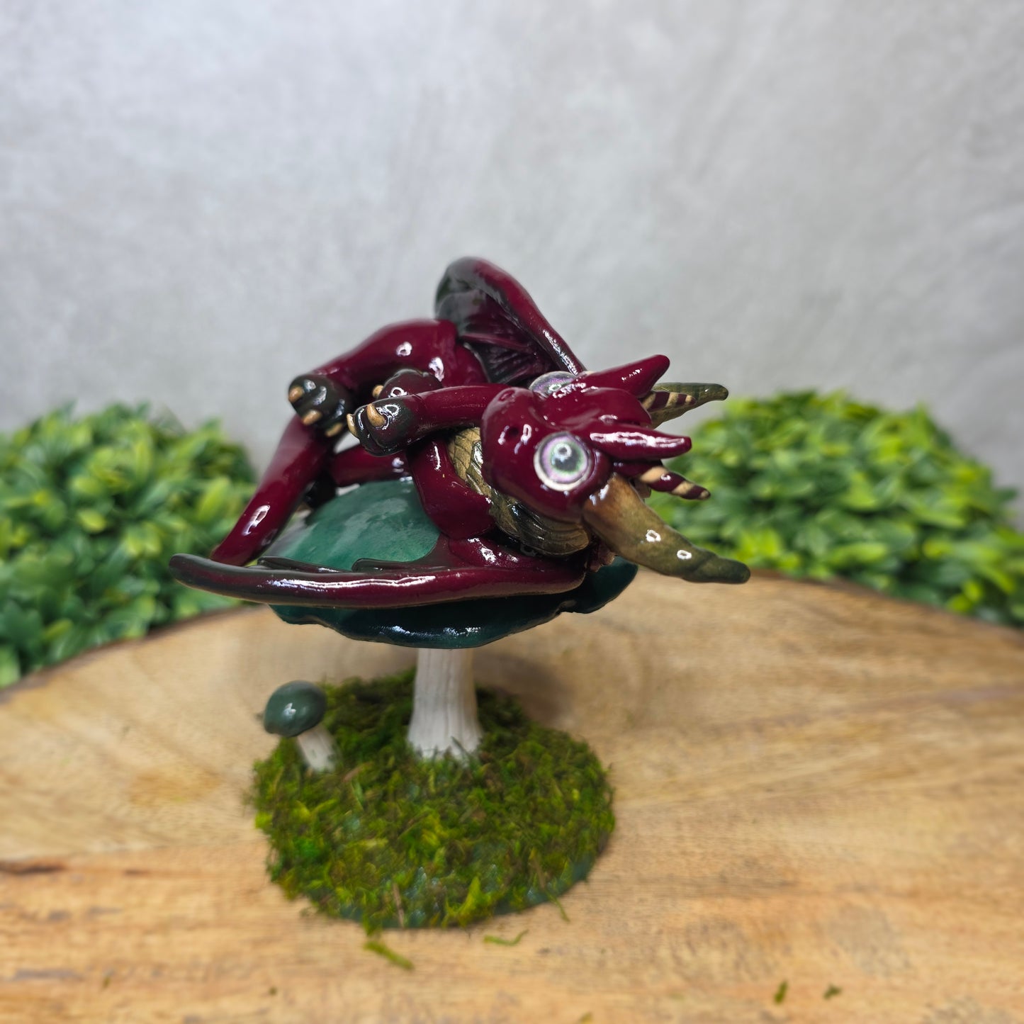 Small dragon figurine on a wooden surface with greenery