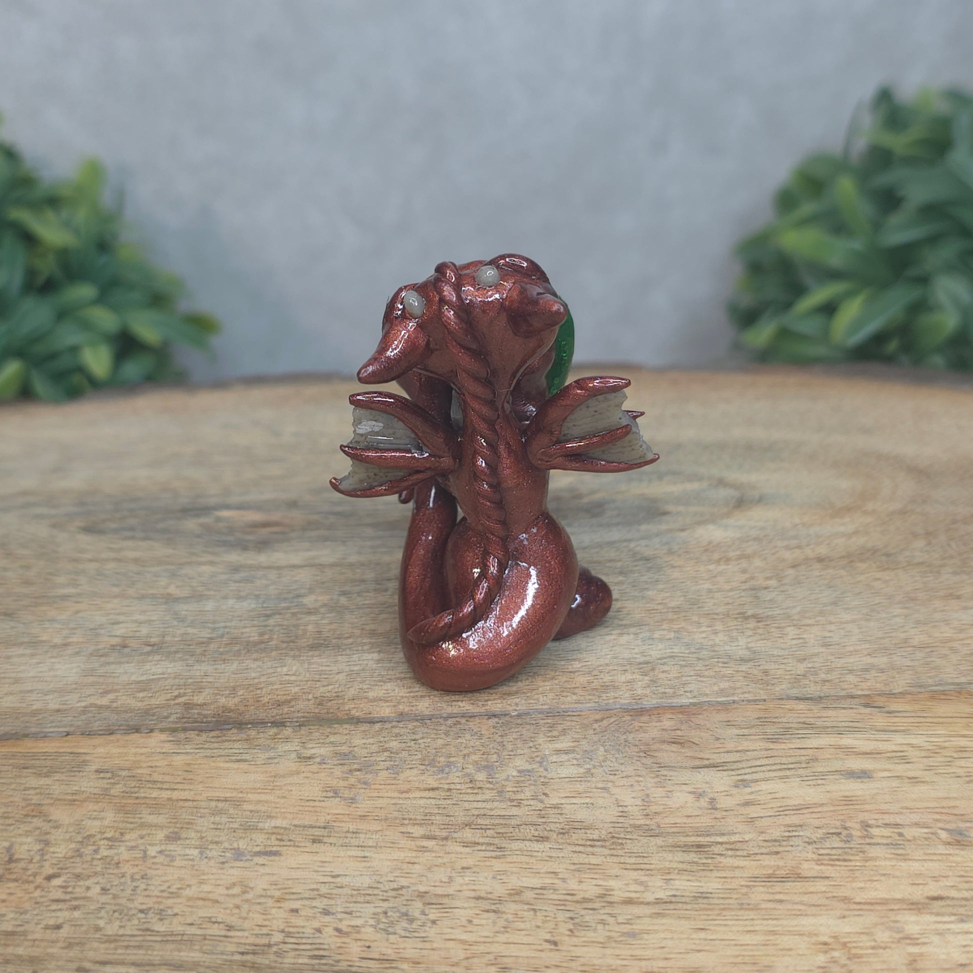 A baby polymer clay dragon with a green heart against a blurred background