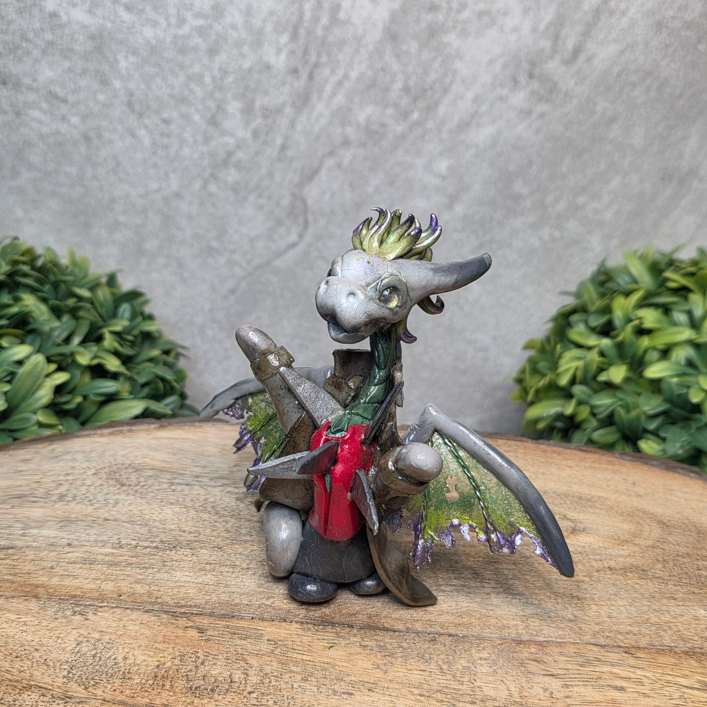 Clay dragon in costume on a wood surface with greenery.
