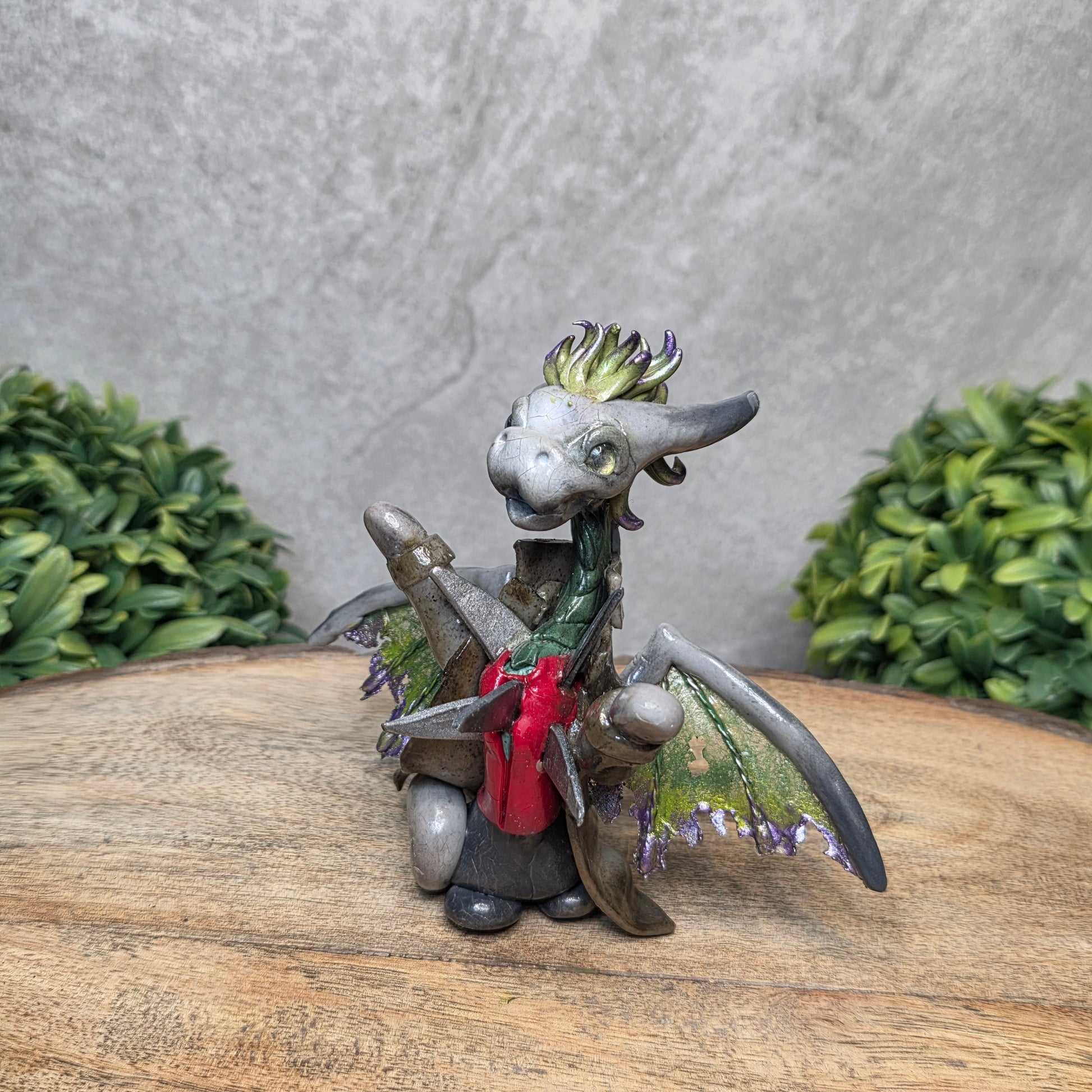 Clay dragon in costume on a wood surface with greenery.