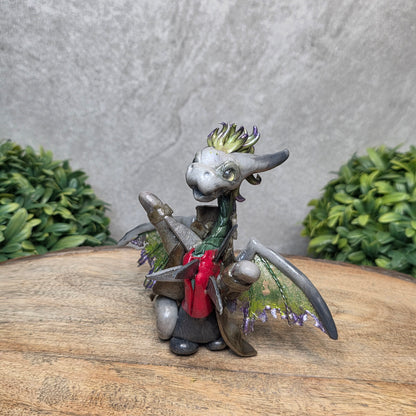 Clay dragon in costume on a wood surface with greenery.