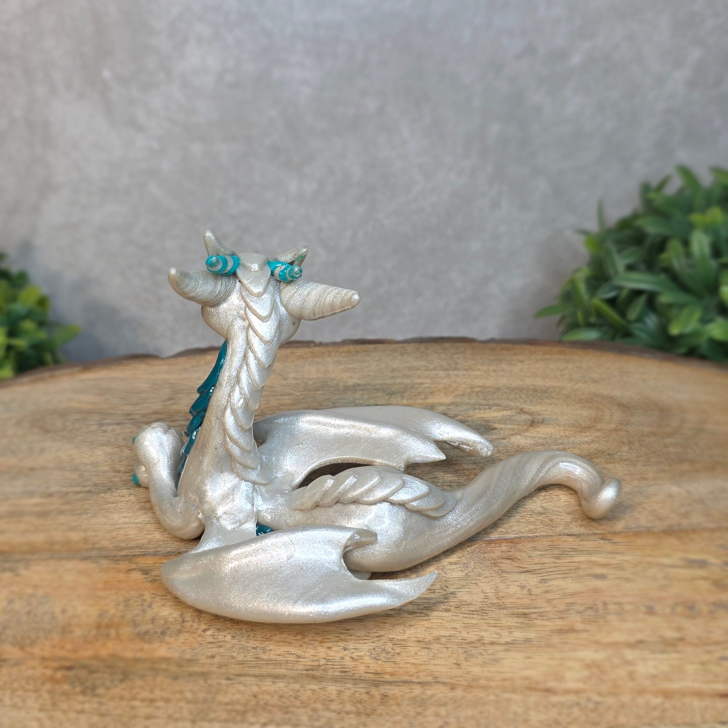 A white and teal clay dragon against a blurred wood surface