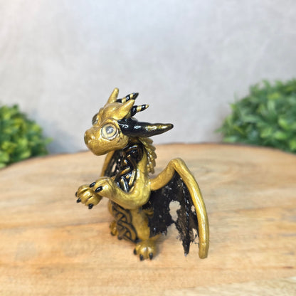 A clay dragon figurine on a wooden surface with a blurred green plant in the background