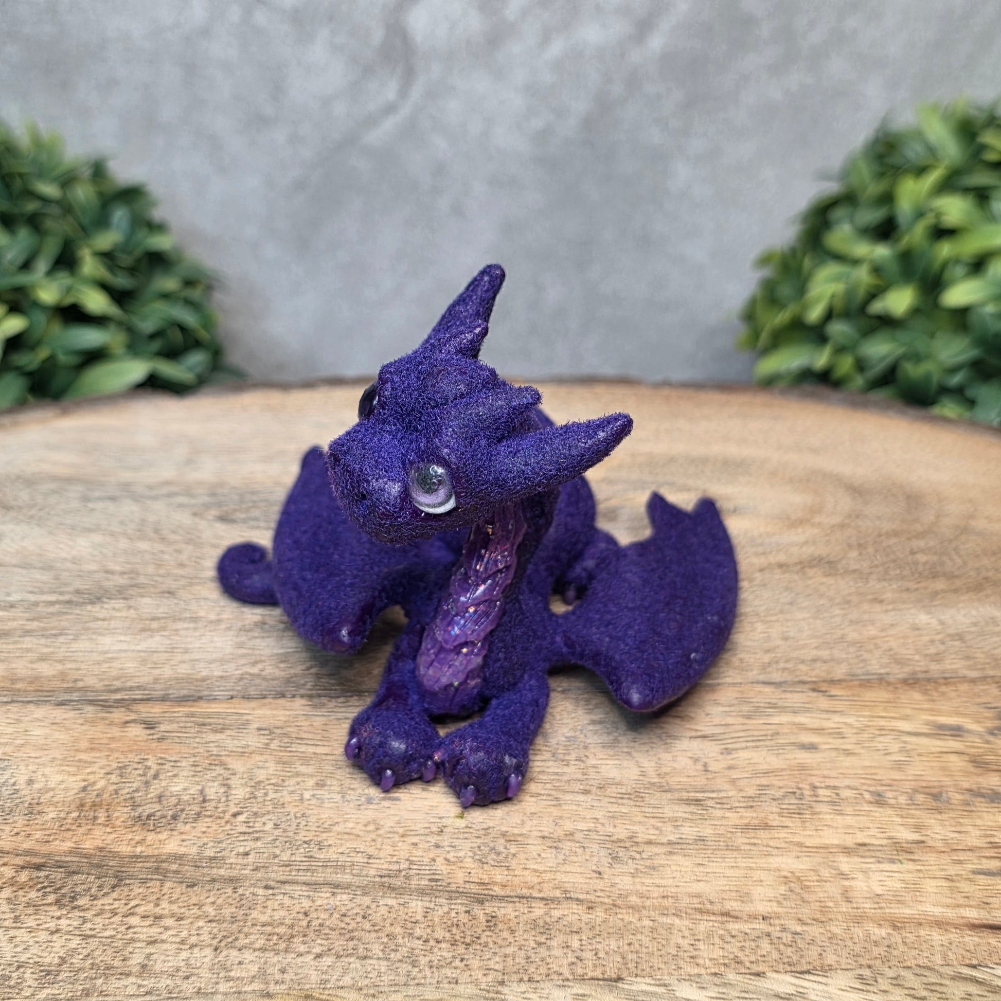 A flocked clay dragon sculpture on a wood surface with greenery.