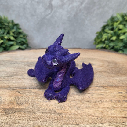 A flocked clay dragon sculpture on a wood surface with greenery.
