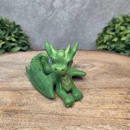A flocked clay dragon sculpture on a wood surface with greenery.