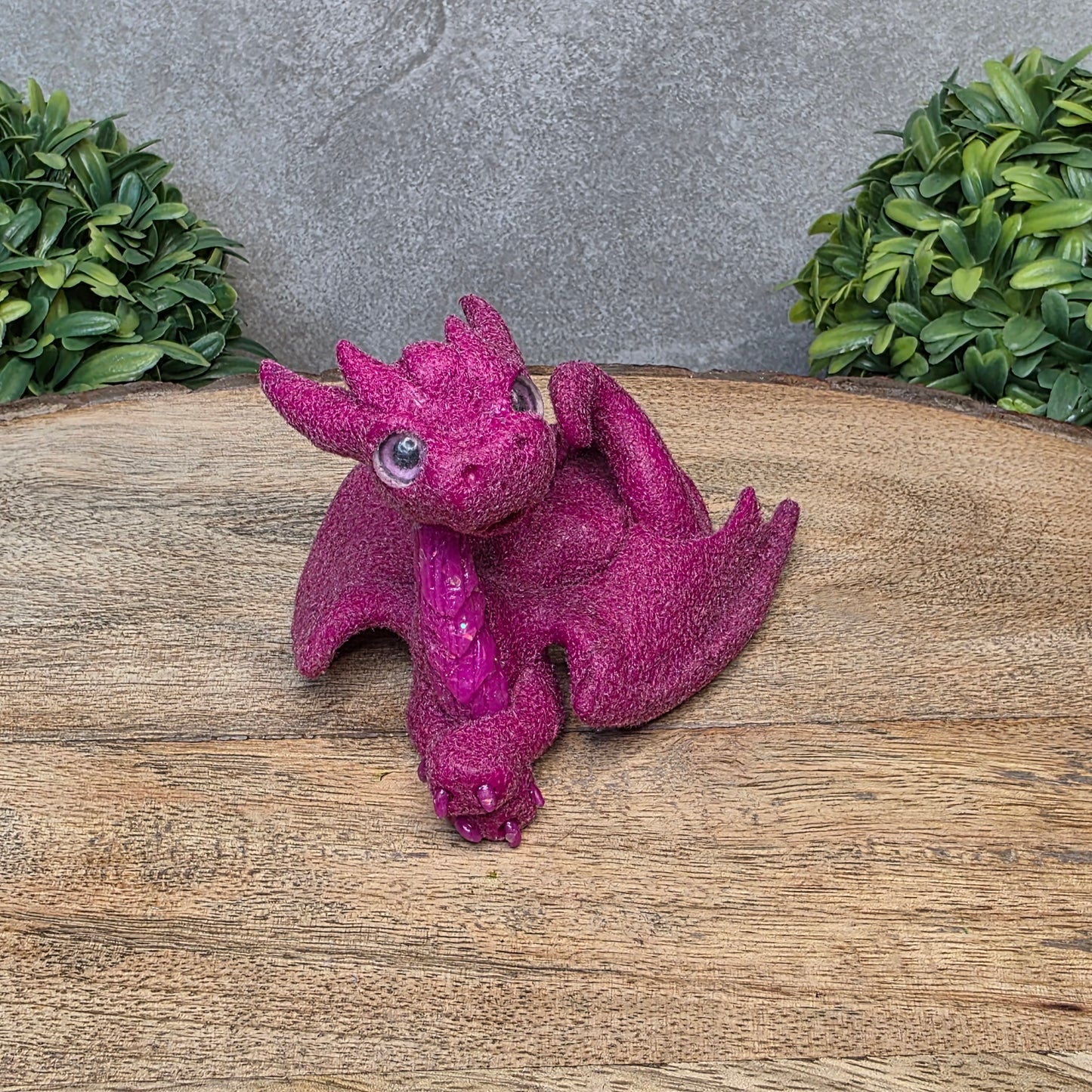 A flocked clay dragon sculpture on a wood surface with greenery.