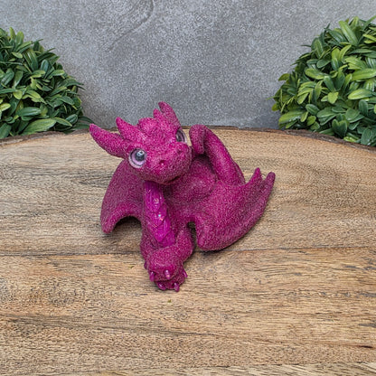 A flocked clay dragon sculpture on a wood surface with greenery.