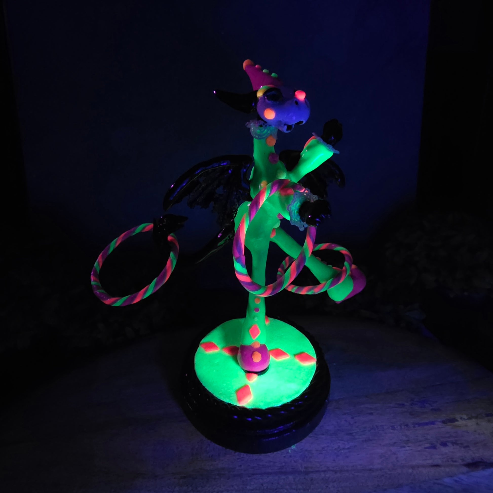 A blacklight reactive clown dragon with hoola hoops on a wood surface with greenery
