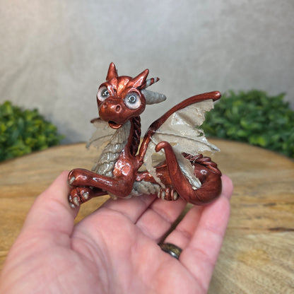 A hand holding a bronze and gray clay dragon against a blurred wood surface