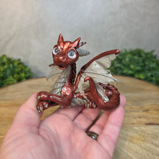 A hand holding a bronze and gray clay dragon against a blurred wood surface