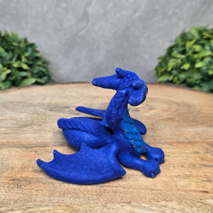 A flocked clay dragon sculpture on a wood surface with greenery.
