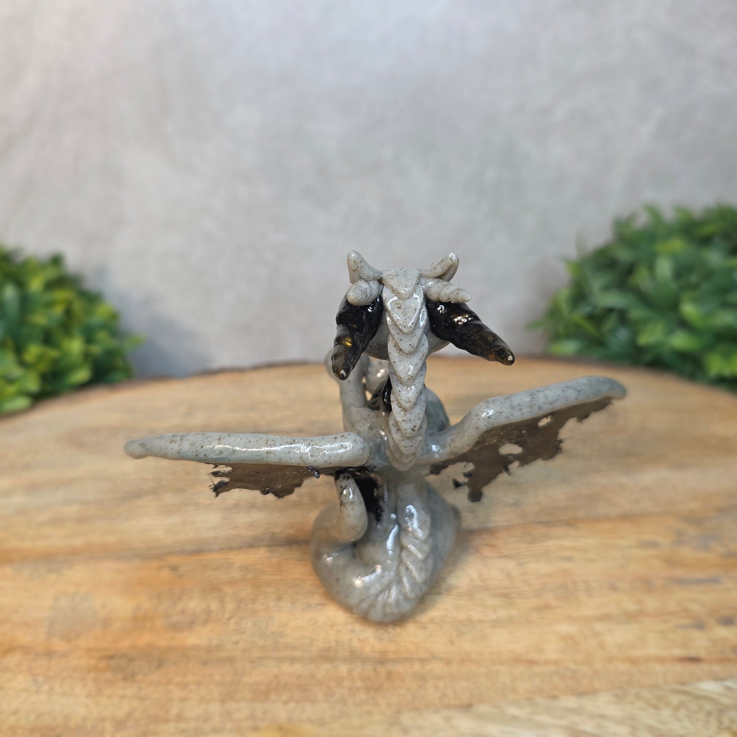 A clay dragon figurine on a wooden surface with a blurred green plant in the background