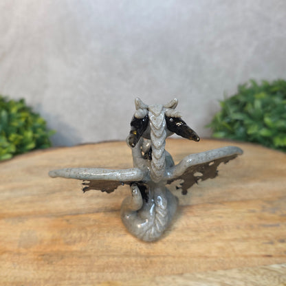 A clay dragon figurine on a wooden surface with a blurred green plant in the background