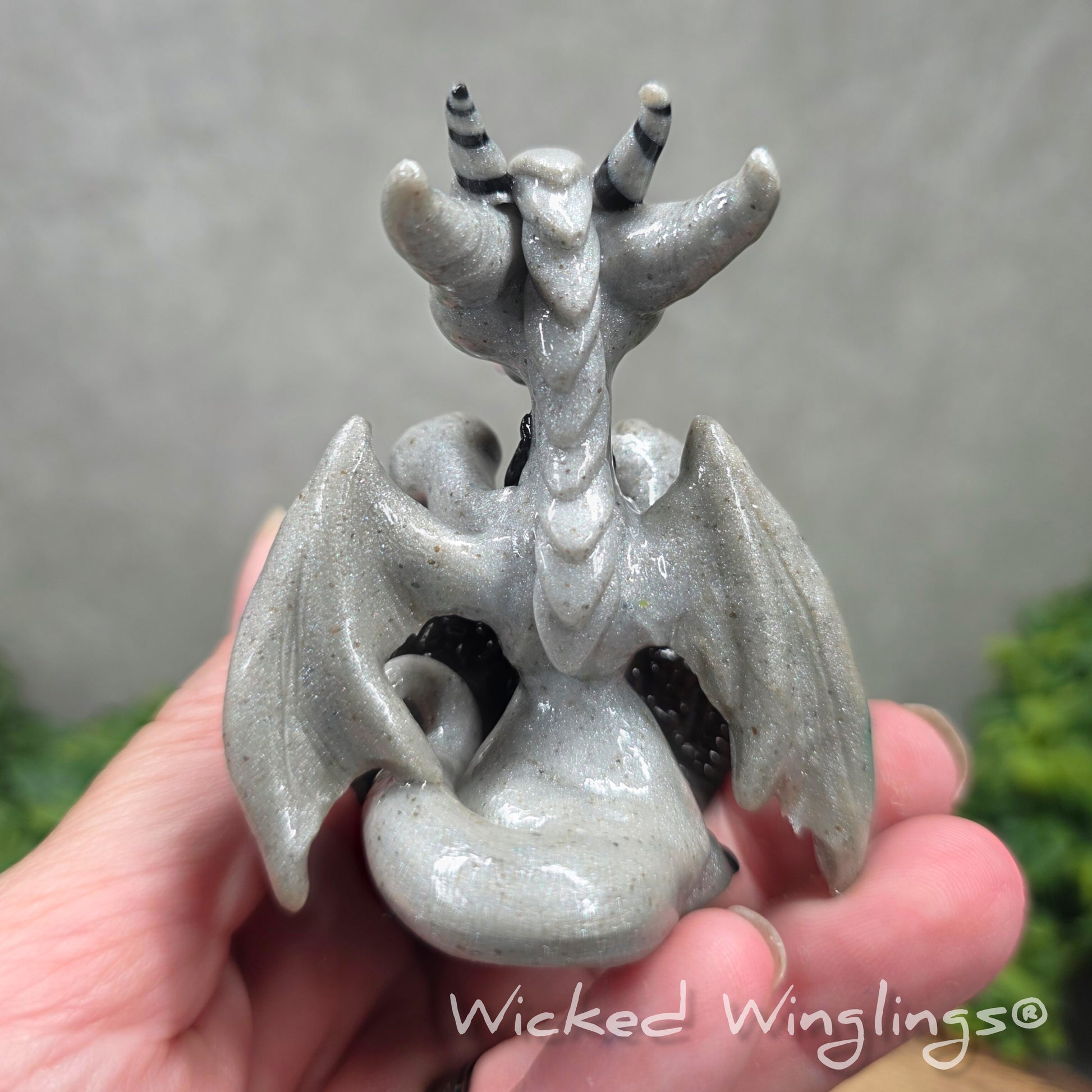 Back view of a hand holding a clay dragon with a cookie with a Wicked Winglings® watermark.