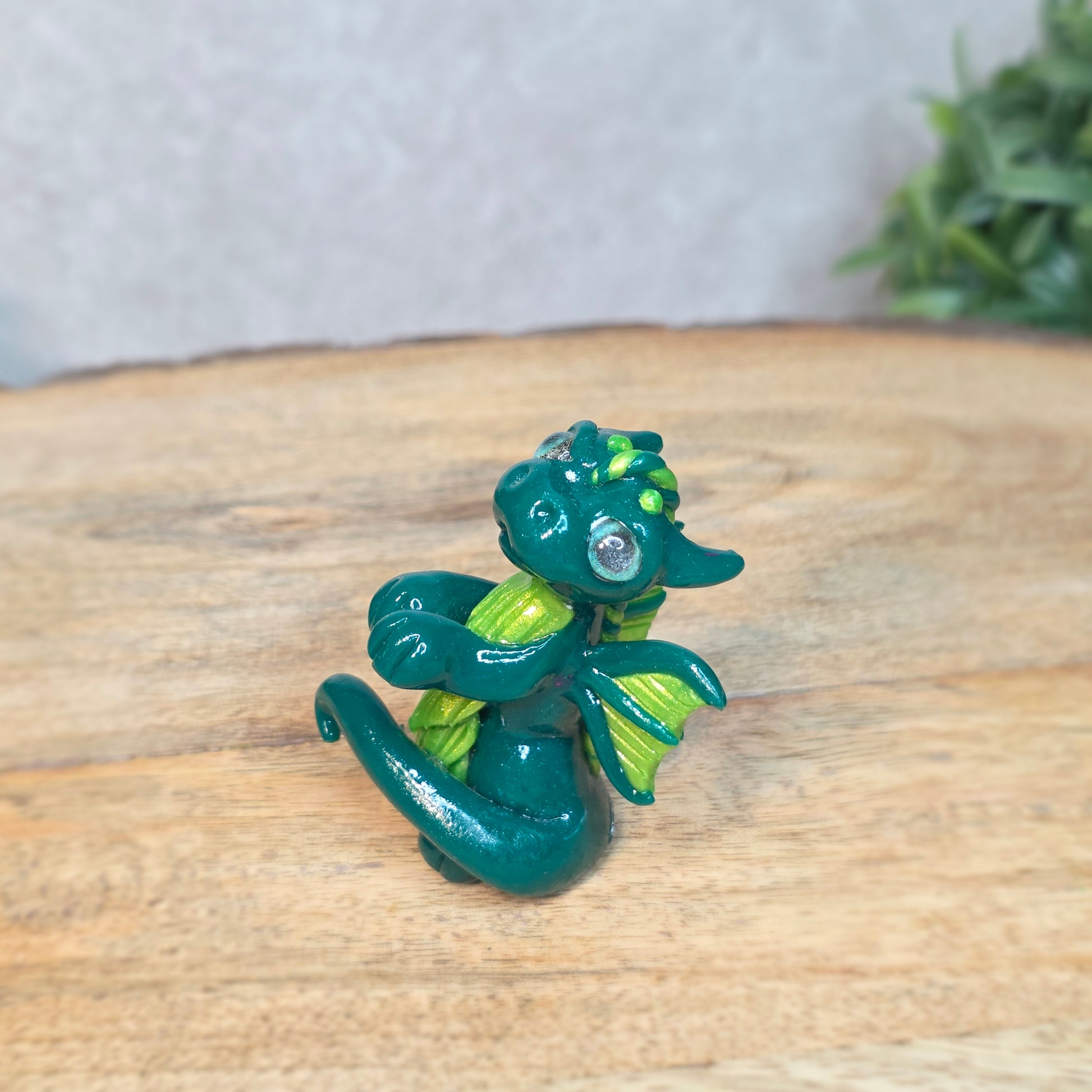 A small green dragon against a blurred wood background
