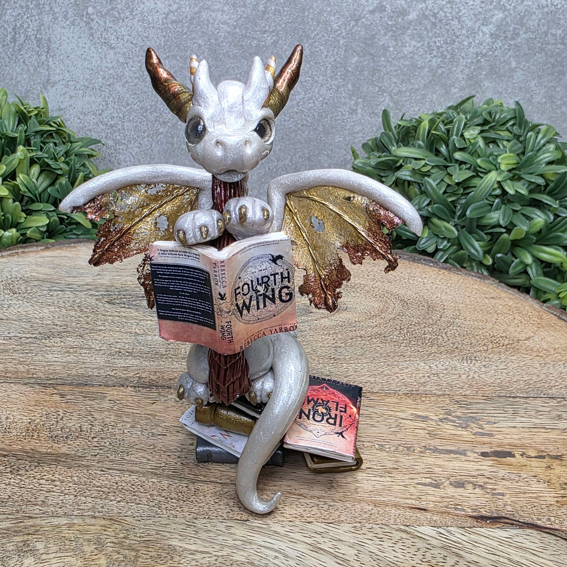 A dragon reading a book against a wood surface with greenery