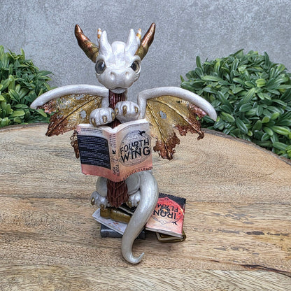 A dragon reading a book against a wood surface with greenery