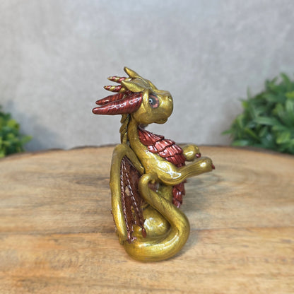 A gold and bronze clay dragon against a blurred wood surface
