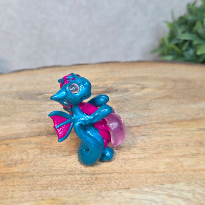 Hand holding a blue and pink clay dragon with a blurred background
