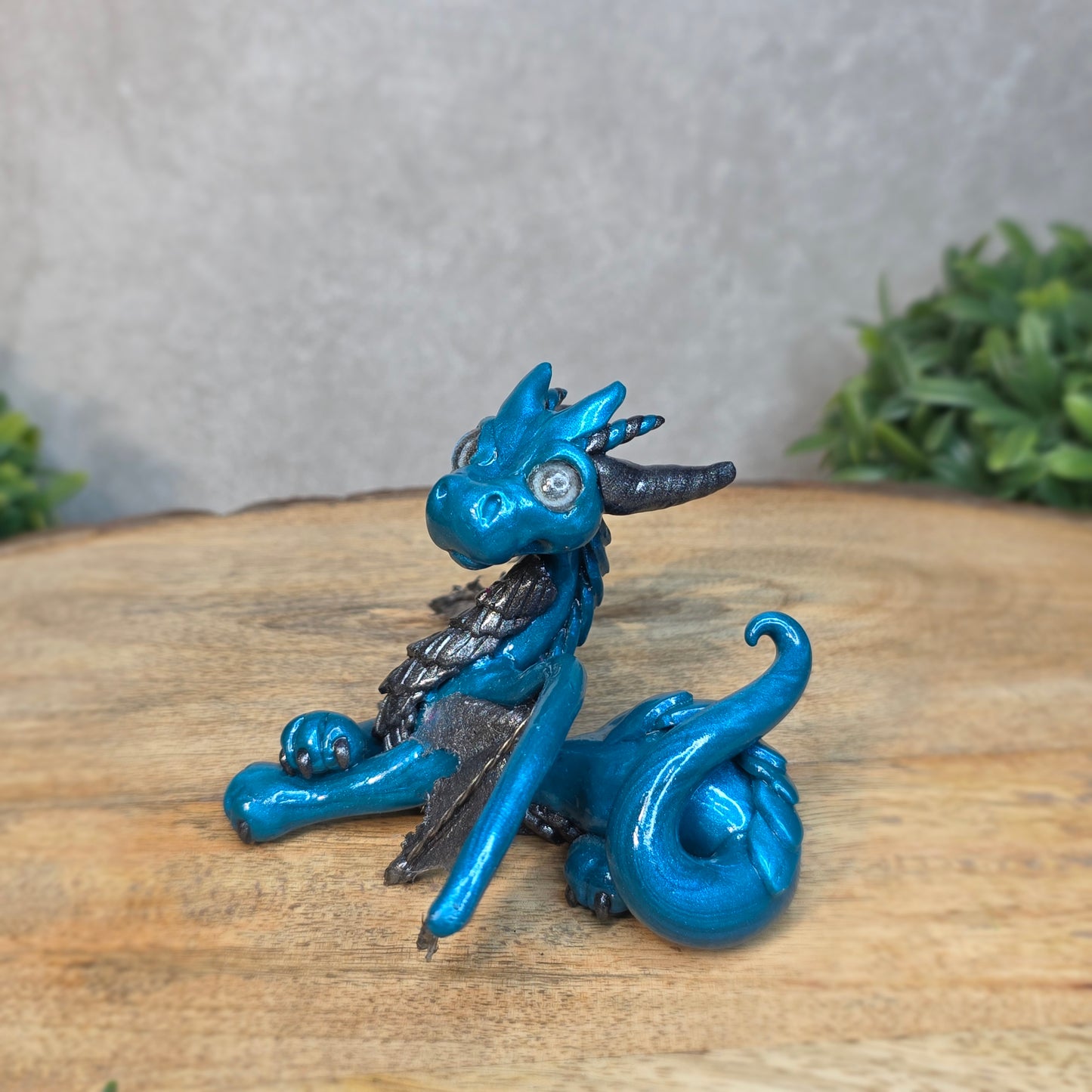 A blue and graphite clay dragon against a blurred wood surface