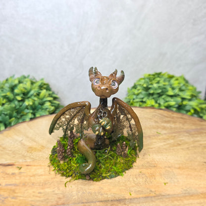 Small dragon figurine on a piece of wood with greenery in the background