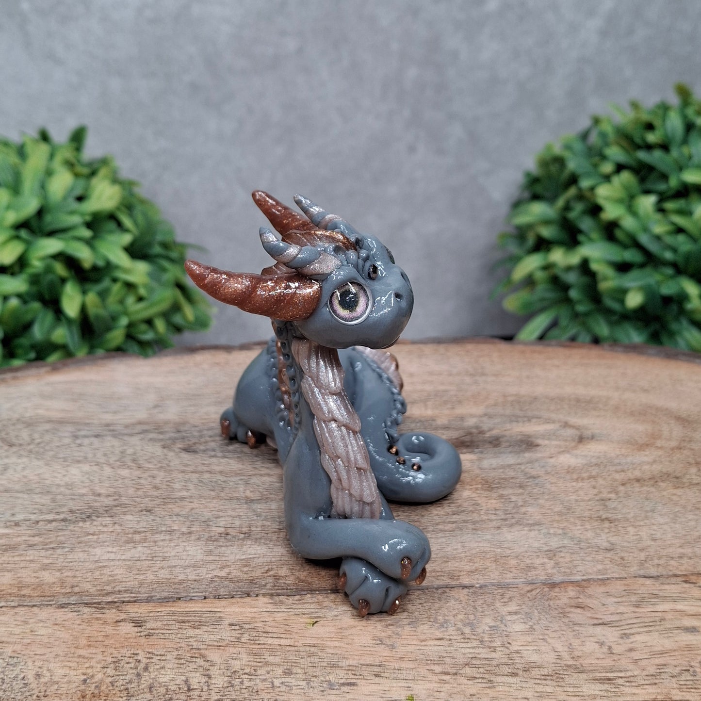 A clay dragon against a wood background with greenery