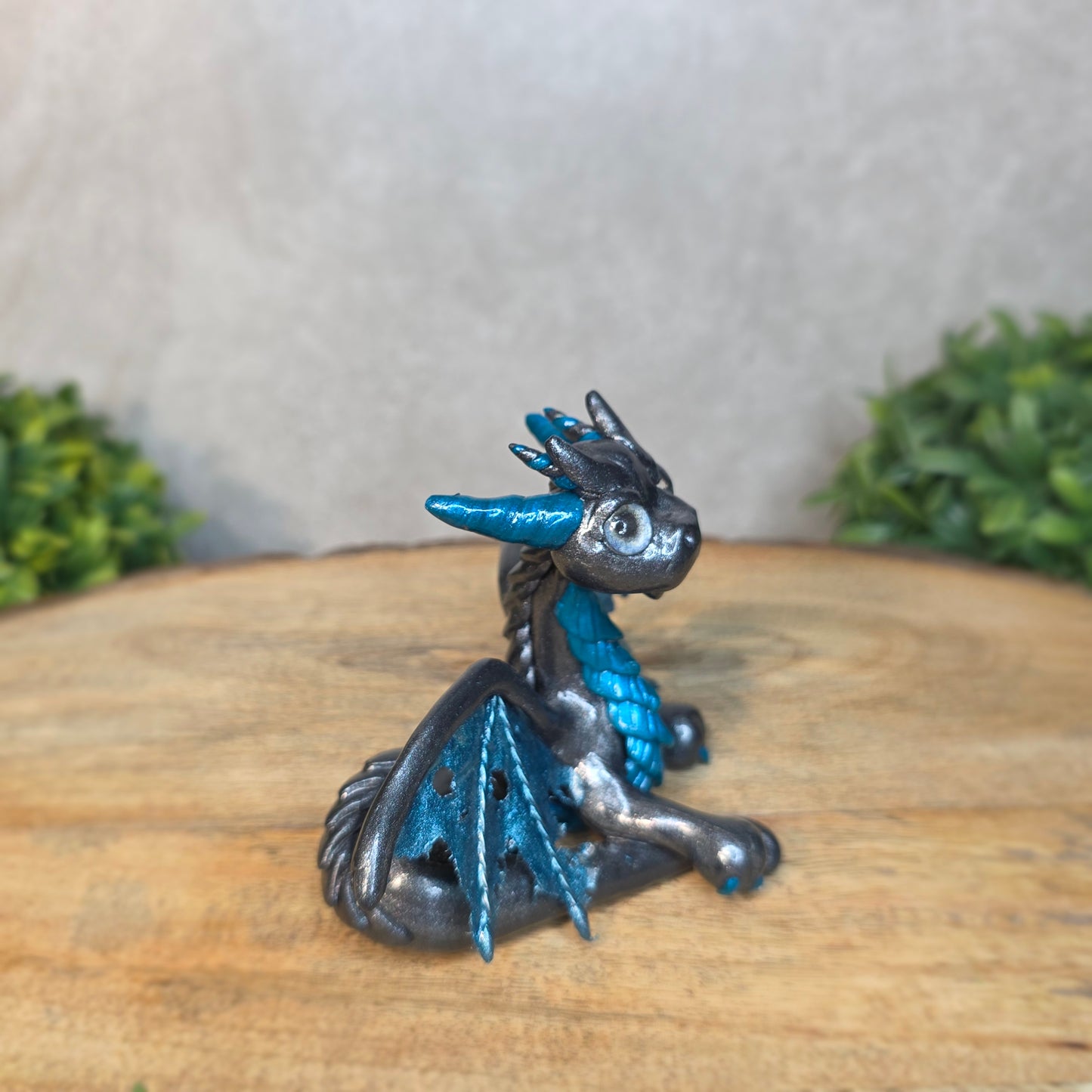 A graphite and blue clay dragon against a blurred wood surface