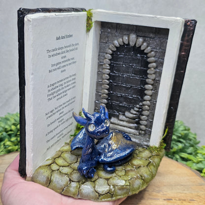 Hand holding a Book nook with dragon on a wood surface with greenery