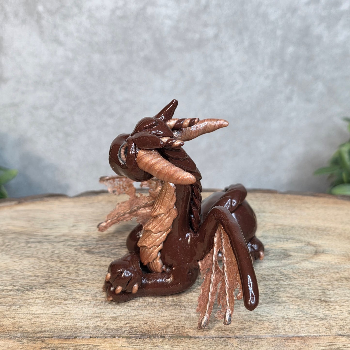 A brown and copper clay dragon against a blurred wood surface