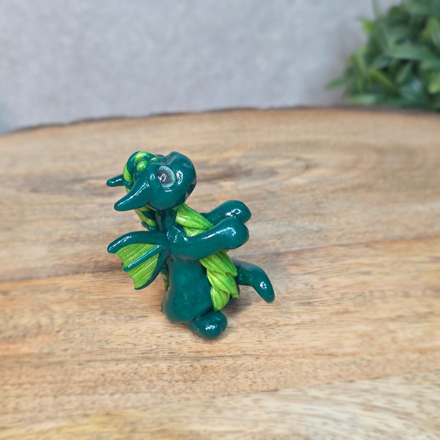 A small green dragon against a blurred wood background