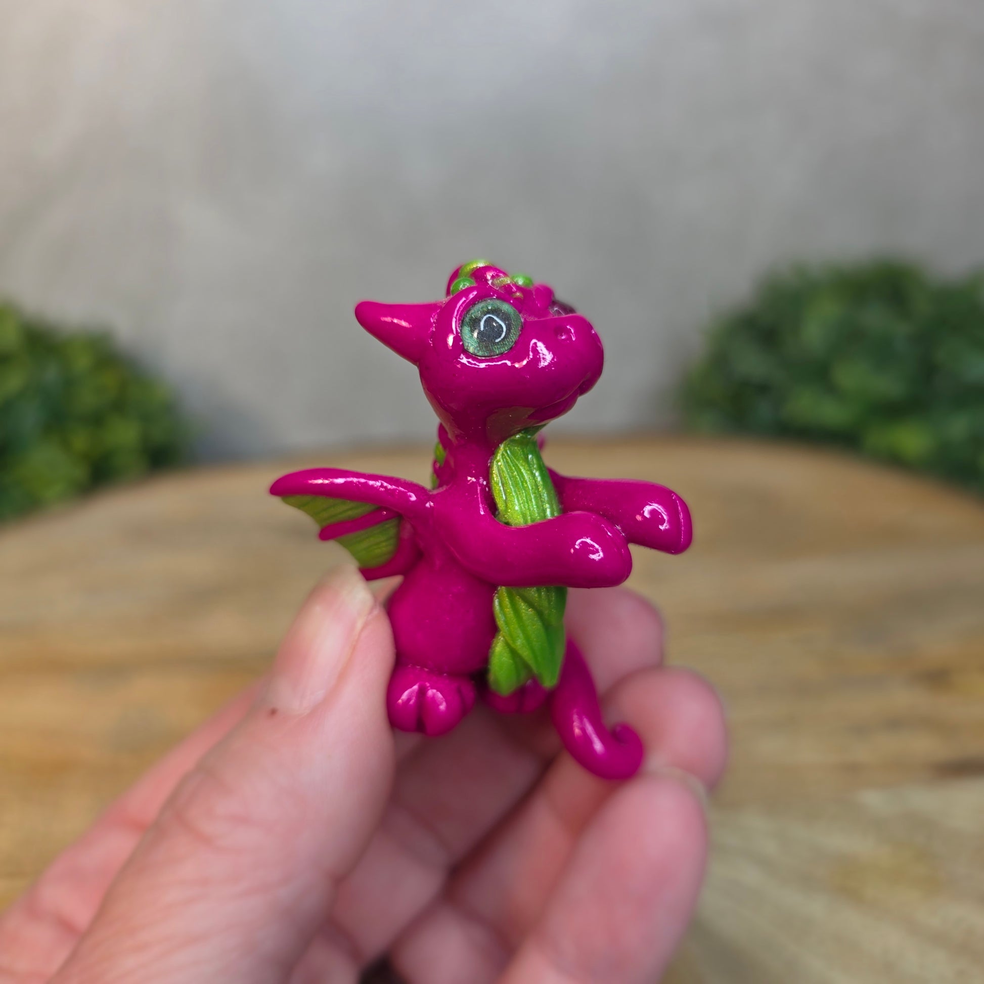 Hand holding a pink and green clay dragon with a blurred background