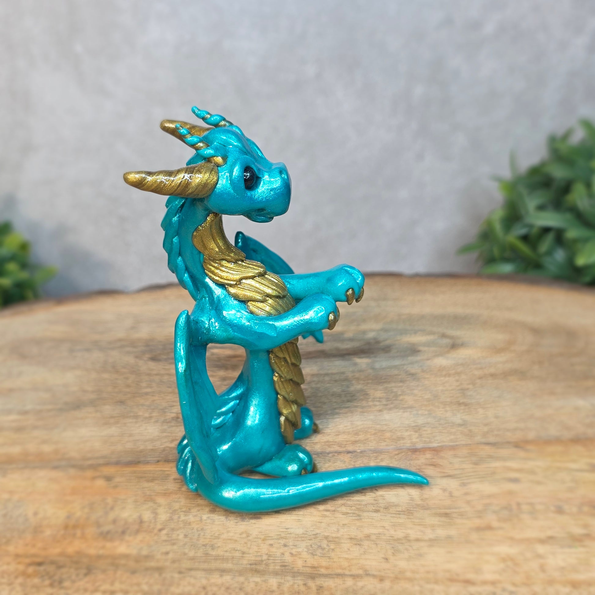 A teal and gold clay dragon against a blurred wood surface