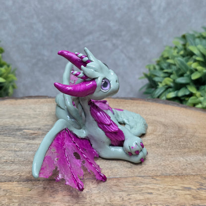 Side view of a clay dragon against a wood surface with greenery.