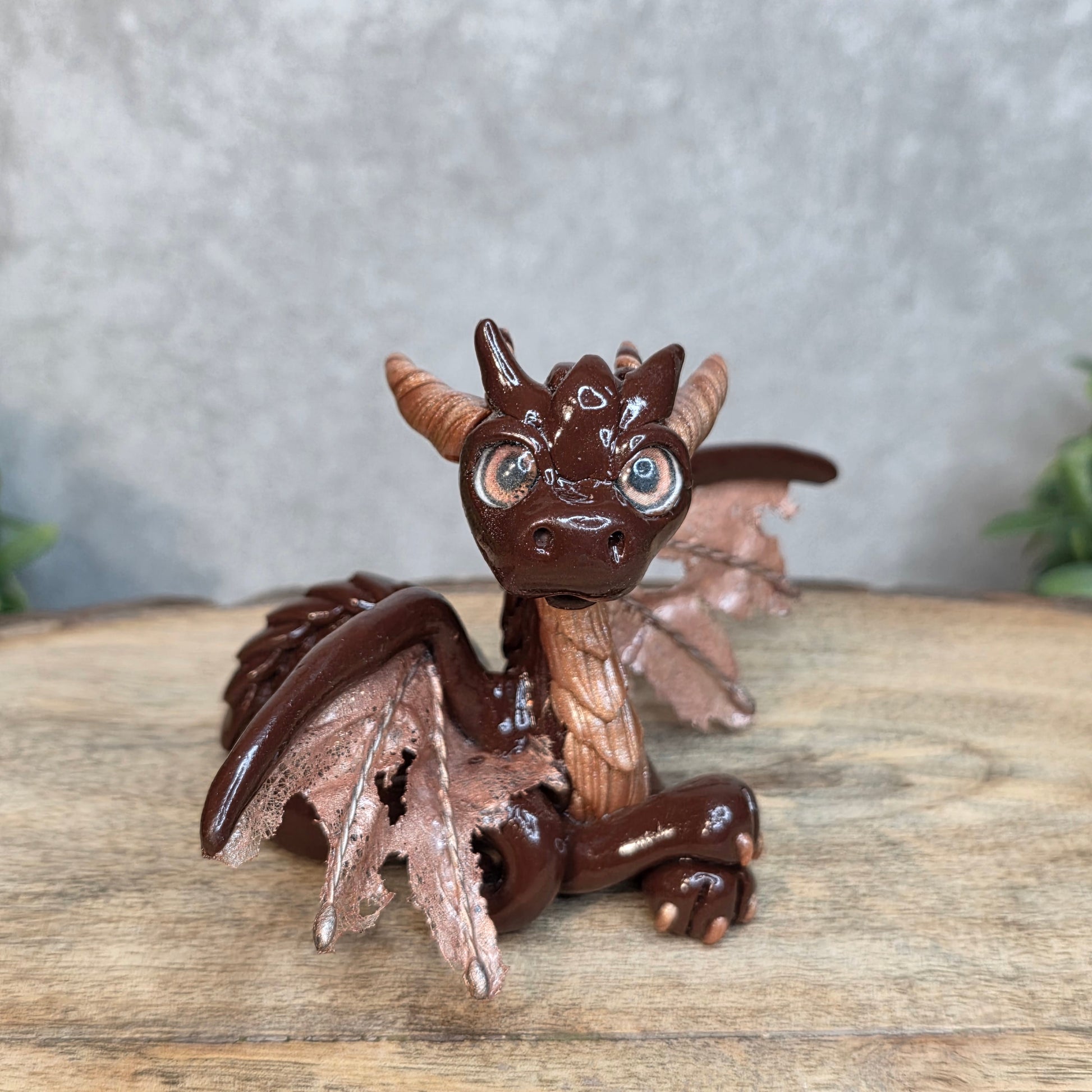 A brown and copper clay dragon against a blurred wood surface