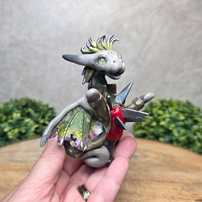 A hand holding a clay dragon dressed in a costume