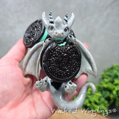 A hand holding a clay dragon with cookies with a Wicked Winglings® watermark.
