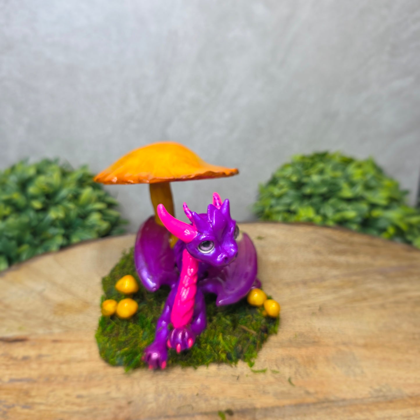 Purple dragon figurine with a yellow mushroom on a wooden surface with greenery