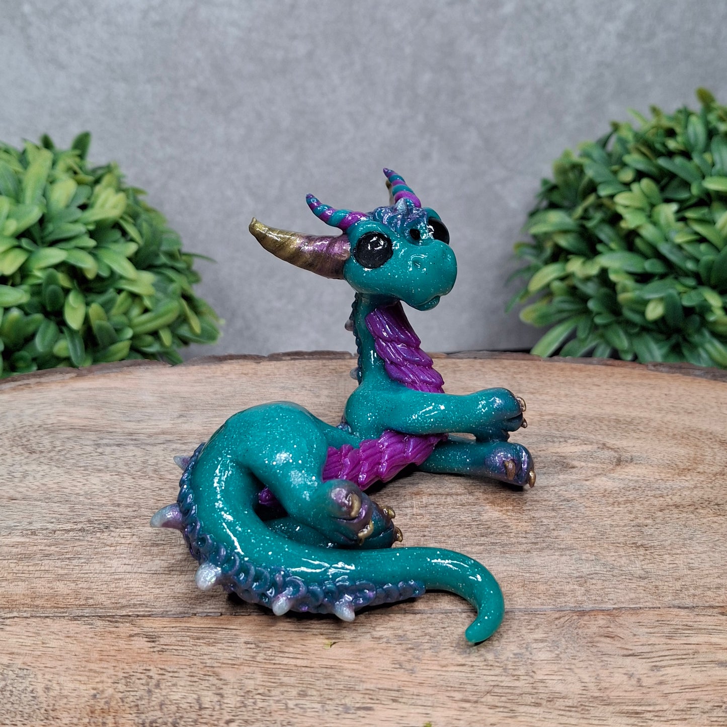 A  clay dragon against a wood background with greenery