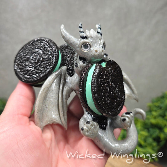 A hand holding a clay dragon with a cookies with a Wicked Winglings® watermark.