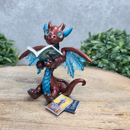 A dragon reading a book against a wood surface with greenery