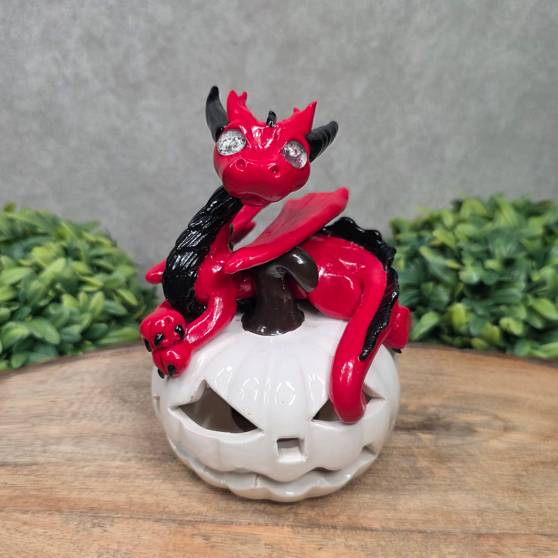 A red dragon sculpture on a white jack o lantern with greenery