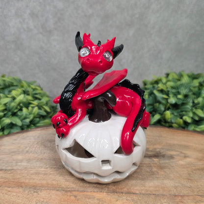A red dragon sculpture on a white jack o lantern with greenery
