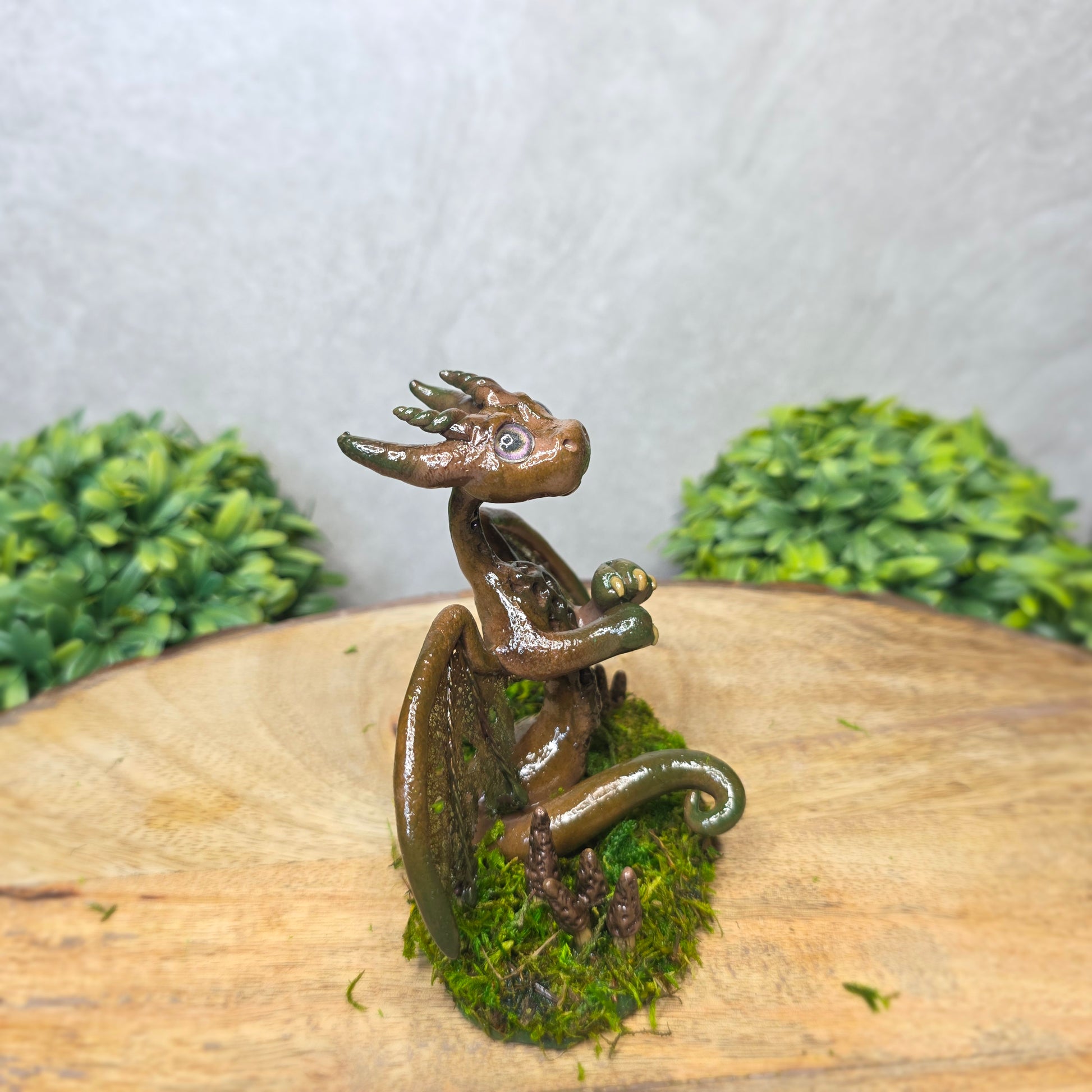 Small dragon figurine on a piece of wood with greenery in the background